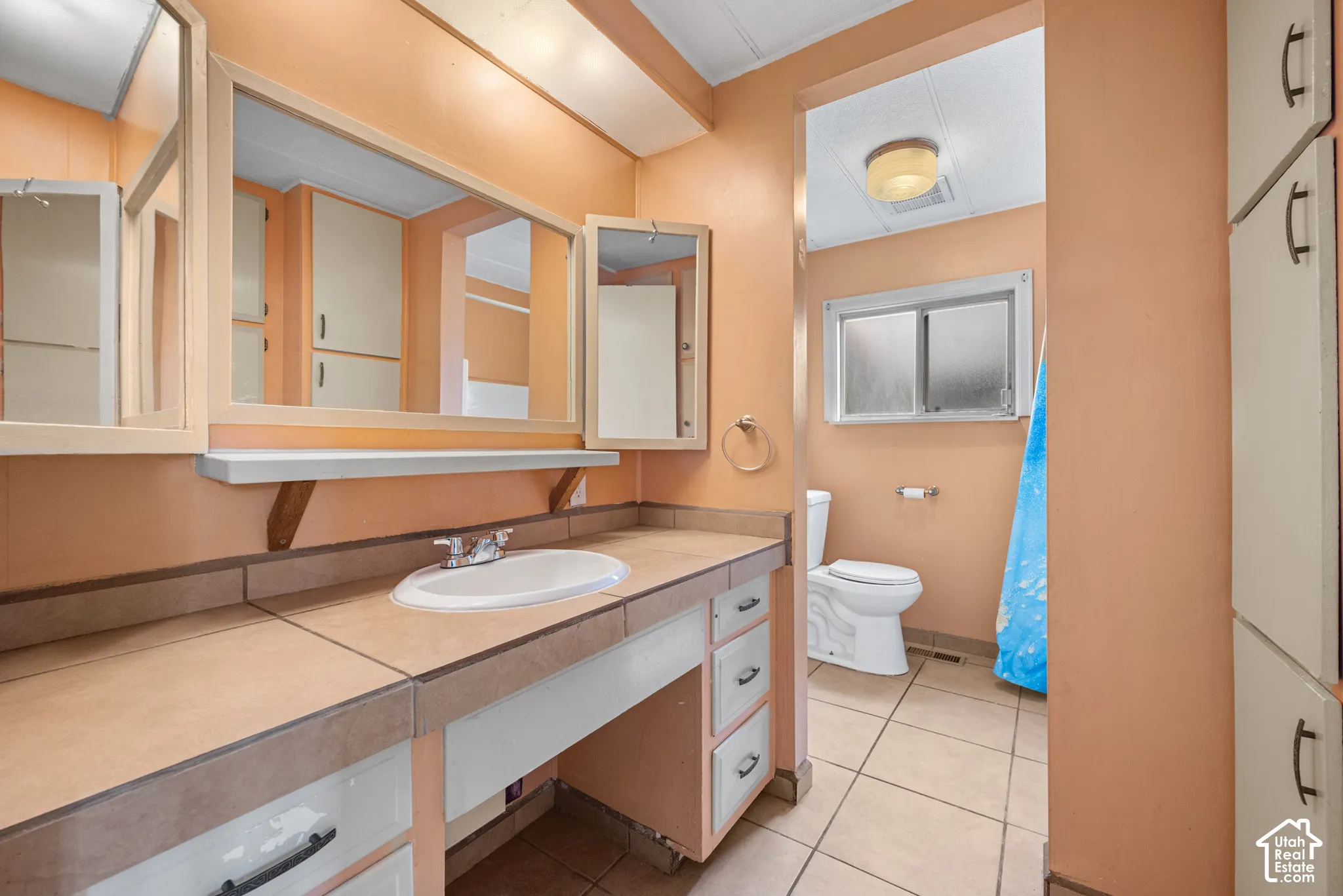 Bathroom featuring a tile-topped vanity with an integrated basin, large triple-pane mirror, built-in floor-to-ceiling cabinetry, ceramic tile flooring, and a sliding window