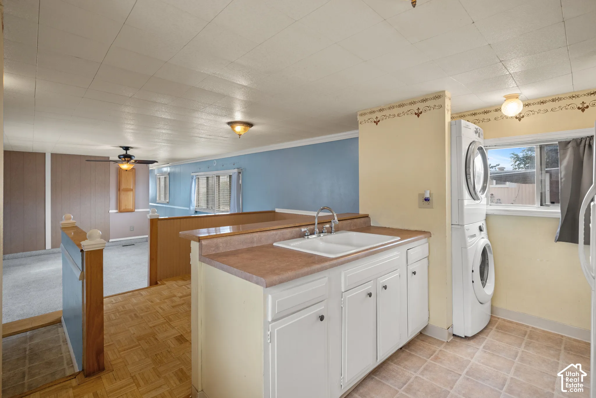 Utility space featuring a stacked washer and dryer, white cabinetry, a dual-basin drop-in sink with a chrome faucet, and tile-finish flooring
