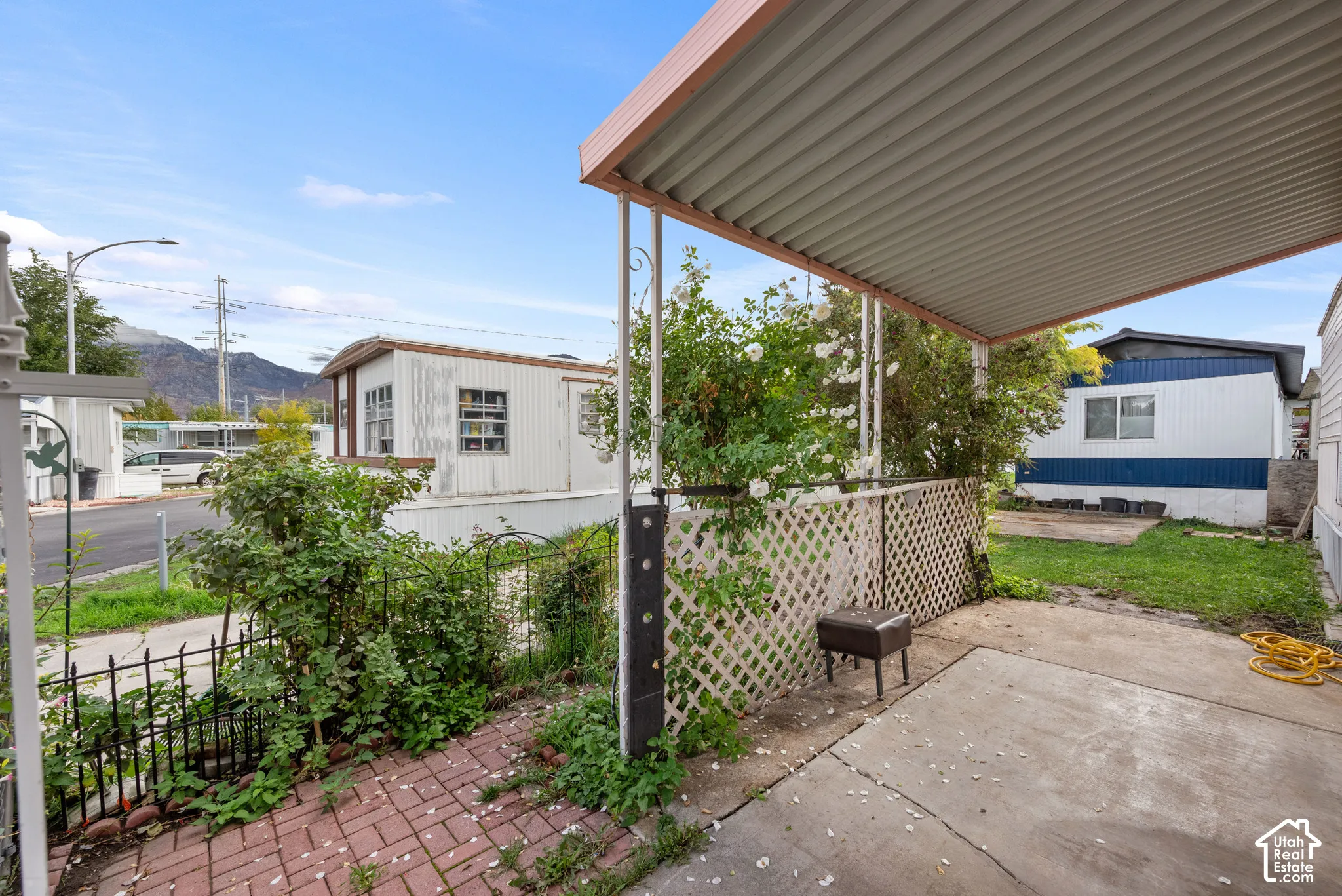 Covered carport featuring a concrete pad, metal roof canopy, white diamond-pattern lattice privacy screening, and brick paver accents