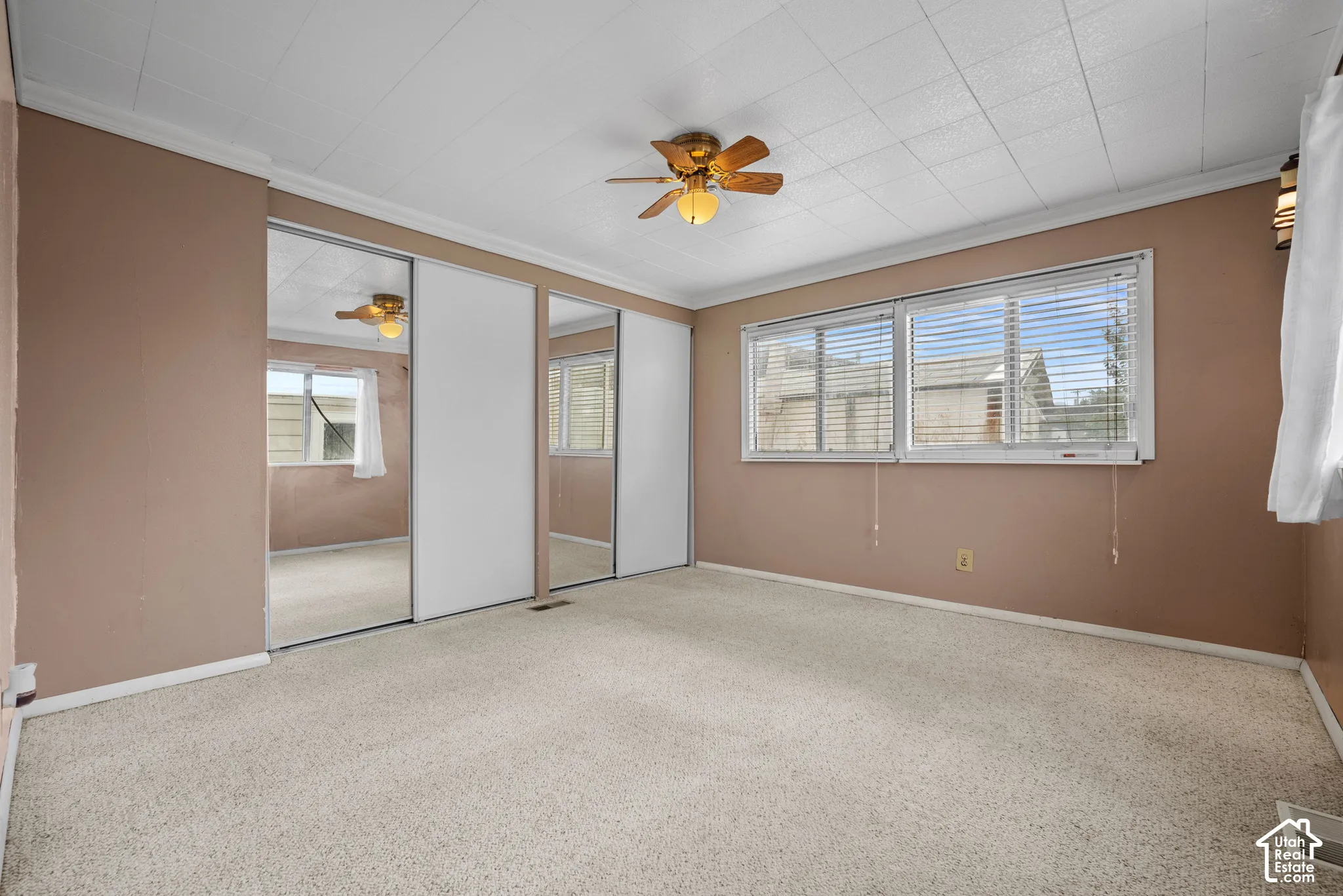 Room featuring wall-to-wall carpeting, dual sliding-door mirrored closet, ceiling fan with integrated lighting, and multiple windows