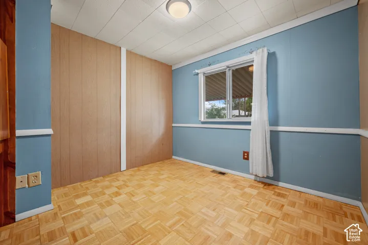 Room featuring wood-finish parquet flooring, paneled wall accents, a grid-patterned drop ceiling, and a central flush-mount light fixture