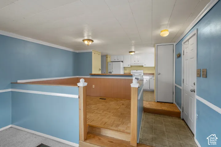 Parquet wood-finish flooring, wood wainscoting, white cabinetry, tiered floor levels, and flush-mount lighting fixtures
