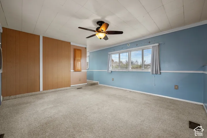 Interior room featuring paneling, painted walls, carpeted flooring, a grid-pattern ceiling, and a central ceiling fan with an integrated light fixture