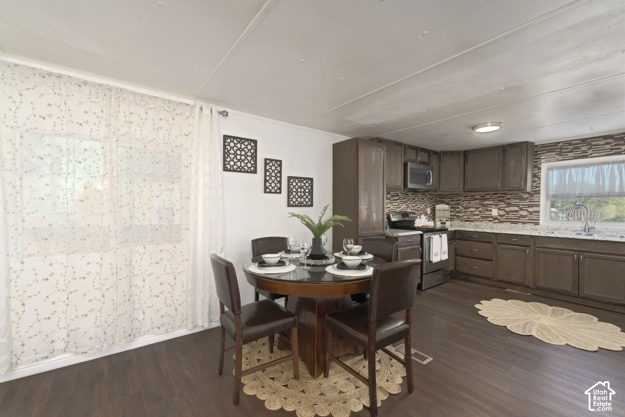 Kitchen featuring dark wood cabinetry, stone-tiled backsplash, light-toned stone countertops, and wood-finish flooring