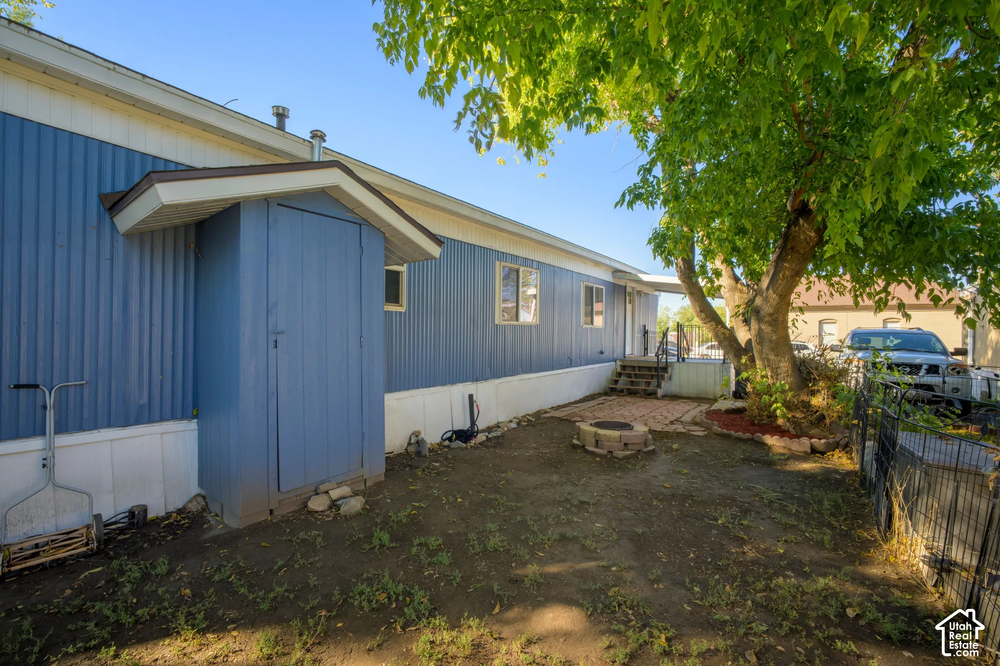 Exterior featuring vertical blue metal siding, a built-in exterior storage closet, a brick-paver patio area, a stone fire pit, and mature shade trees