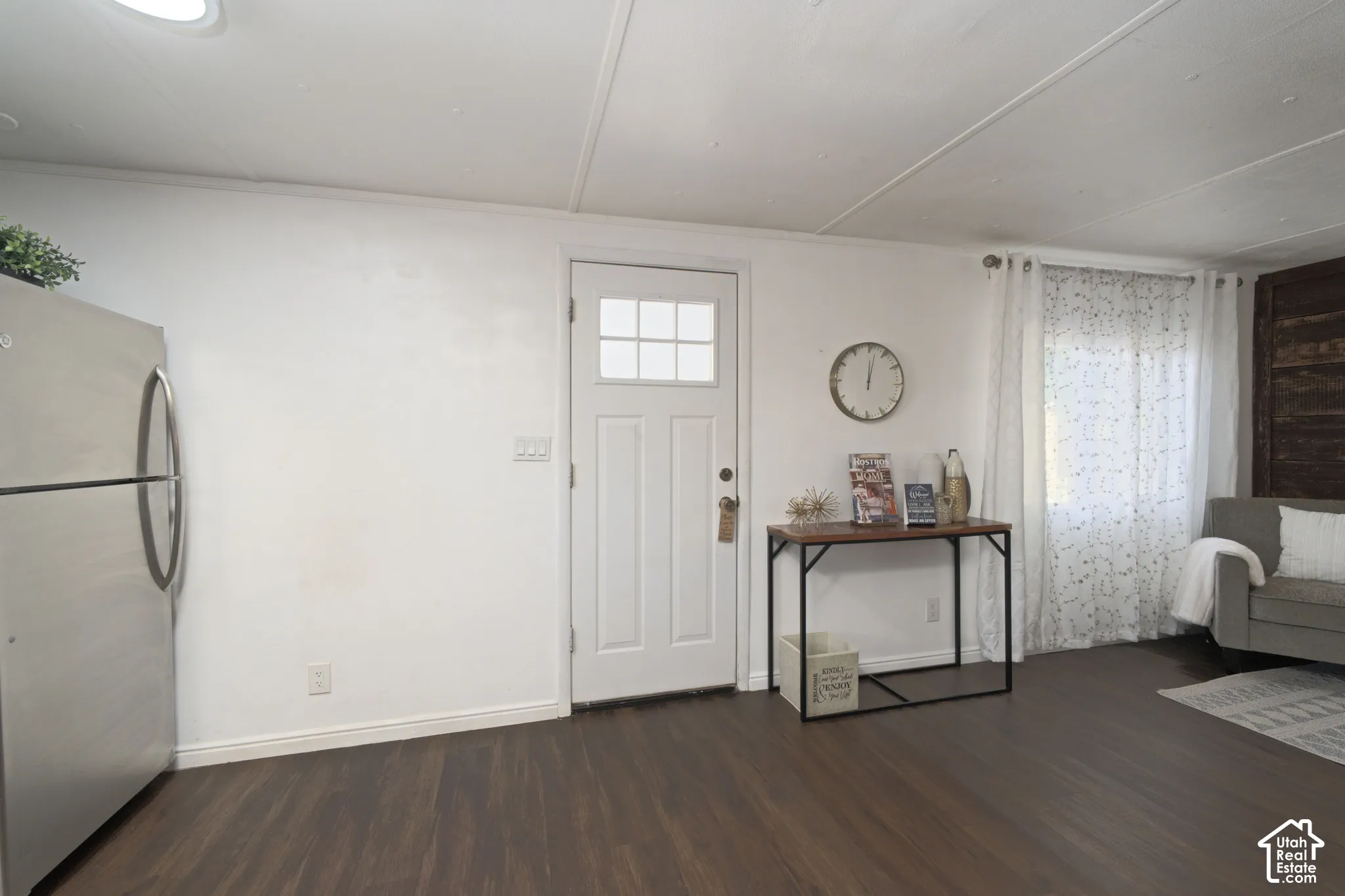 Interior space featuring dark wood-finish flooring, a white exterior-style entry door with a multi-pane glass insert, and a stainless steel refrigerator