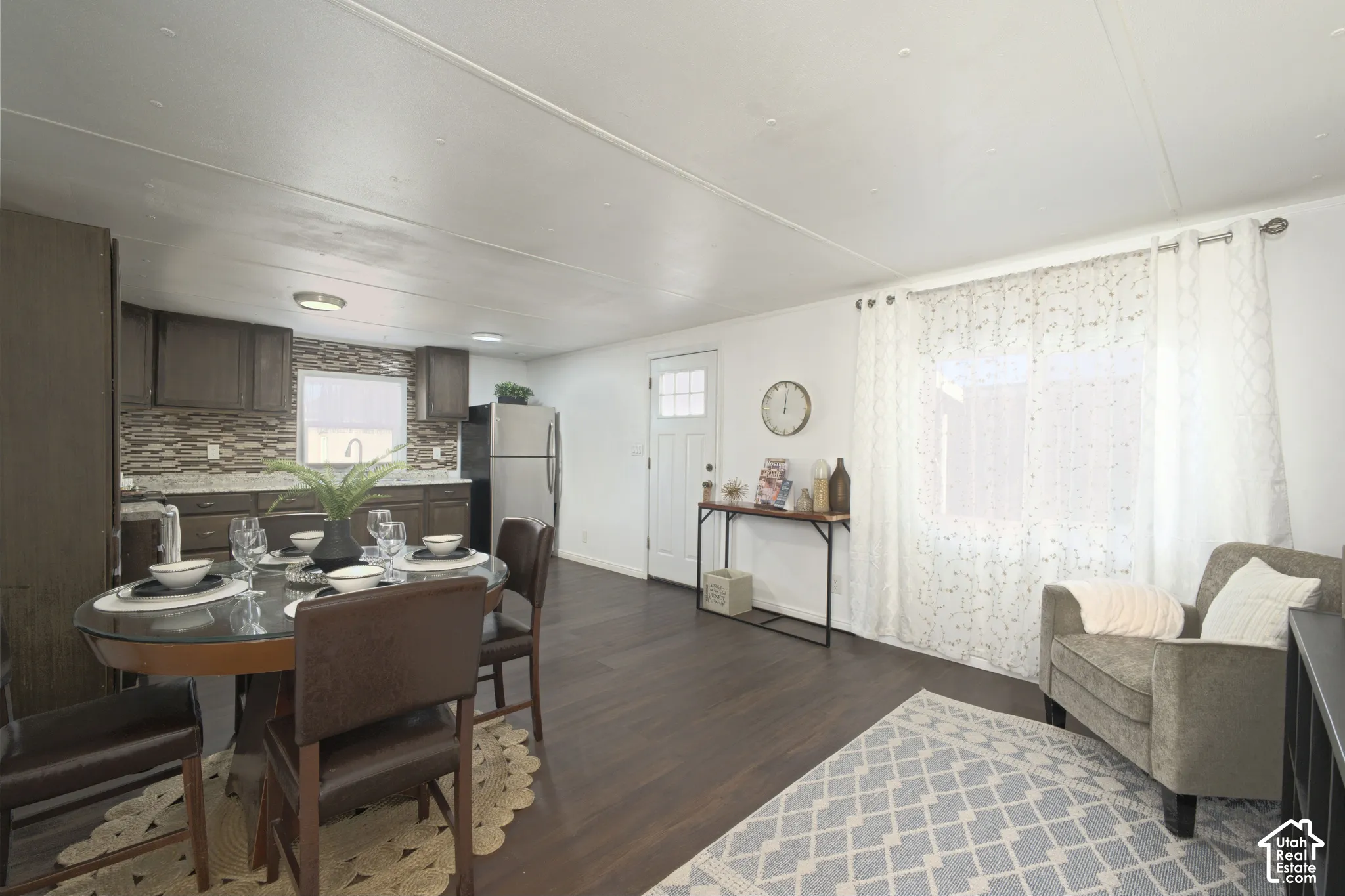 Open-concept space featuring wood-finish flooring, dark-toned cabinetry, multi-textured stone-finish backsplash, and an exterior door with a window insert