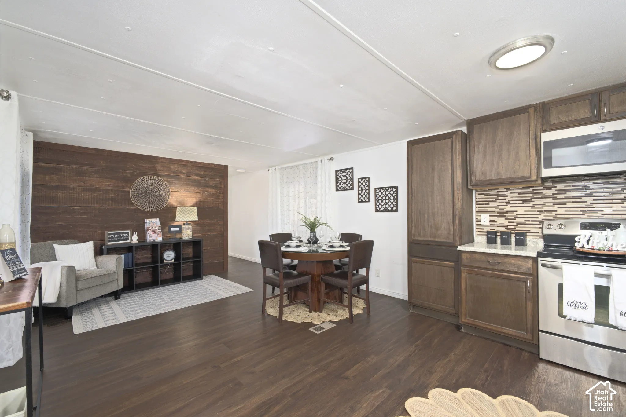 Wood-finish flooring, dark wood-tone cabinetry, stainless steel appliances, stone-textured tile backsplash, and wood-paneled accent wall