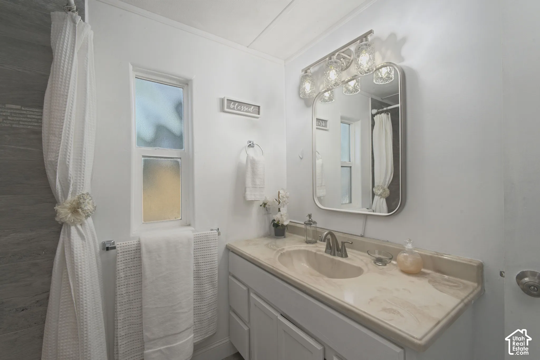 Bathroom vanity with a stone-finish countertop, undermount sink, multi-light vanity fixture, rounded-edge wall mirror, and grey-toned tile surround
