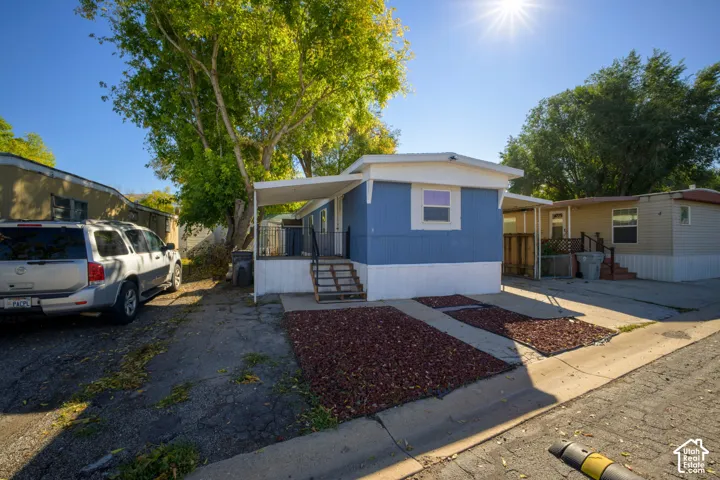 Exterior featuring blue vertical siding, a covered porch with metal railing, asphalt driveway, and ground-level rock landscaping