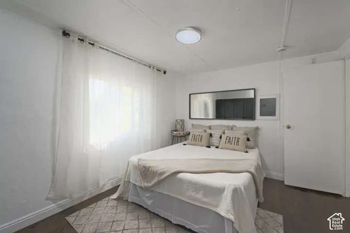 Room featuring wood-finish flooring, white walls, a flush-mount ceiling light fixture, a horizontal wall-mounted mirror, and a window with a curtain rod