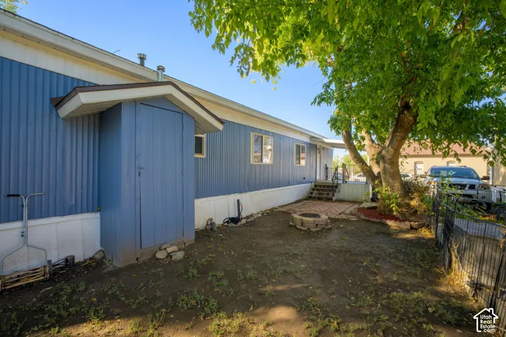 Exterior featuring vertical blue metal siding, a built-in exterior storage closet, a brick-paver patio area, a stone fire pit, and mature shade trees