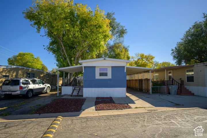 Exterior featuring a blue metal-sided facade, covered carport, metal awning, and wood privacy fencing