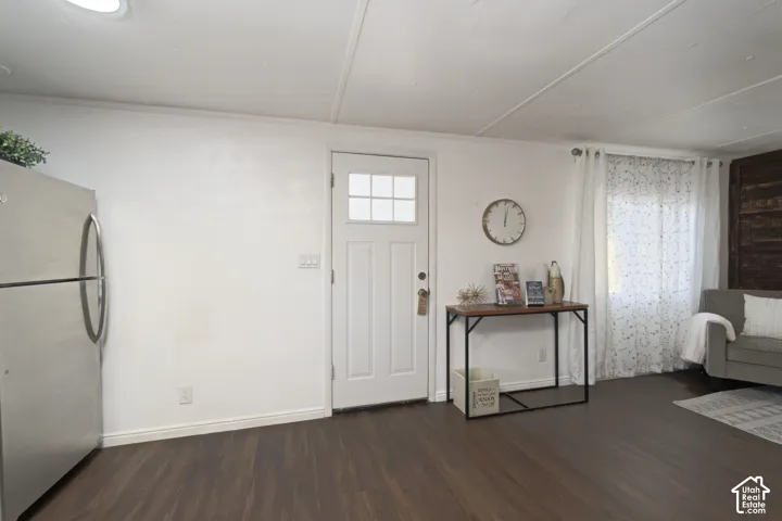 Interior space featuring dark wood-finish flooring, a white exterior-style entry door with a multi-pane glass insert, and a stainless steel refrigerator