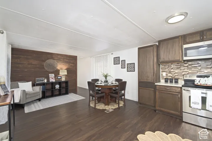 Wood-finish flooring, dark wood-tone cabinetry, stainless steel appliances, stone-textured tile backsplash, and wood-paneled accent wall