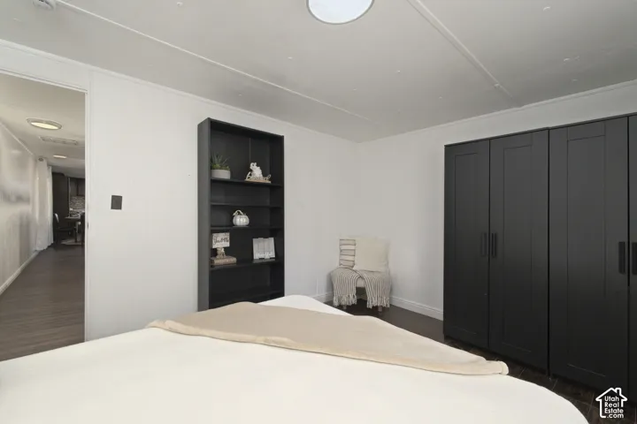 Room featuring dark wood-finish flooring, built-in shelving, and a dark matte-finish wardrobe