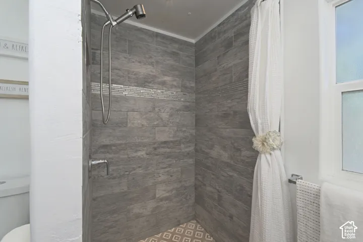 Shower enclosure featuring full-height wood-finish tile surround, integrated decorative accent tile, brushed-finish adjustable shower head, and patterned floor tile