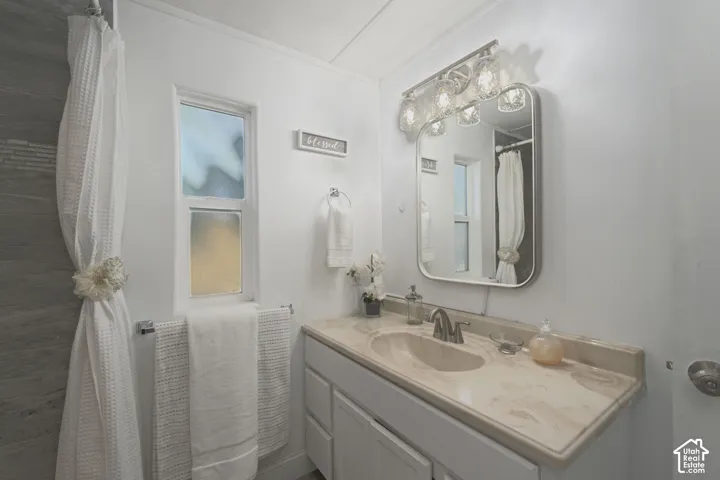 Bathroom vanity with a stone-finish countertop, undermount sink, multi-light vanity fixture, rounded-edge wall mirror, and grey-toned tile surround