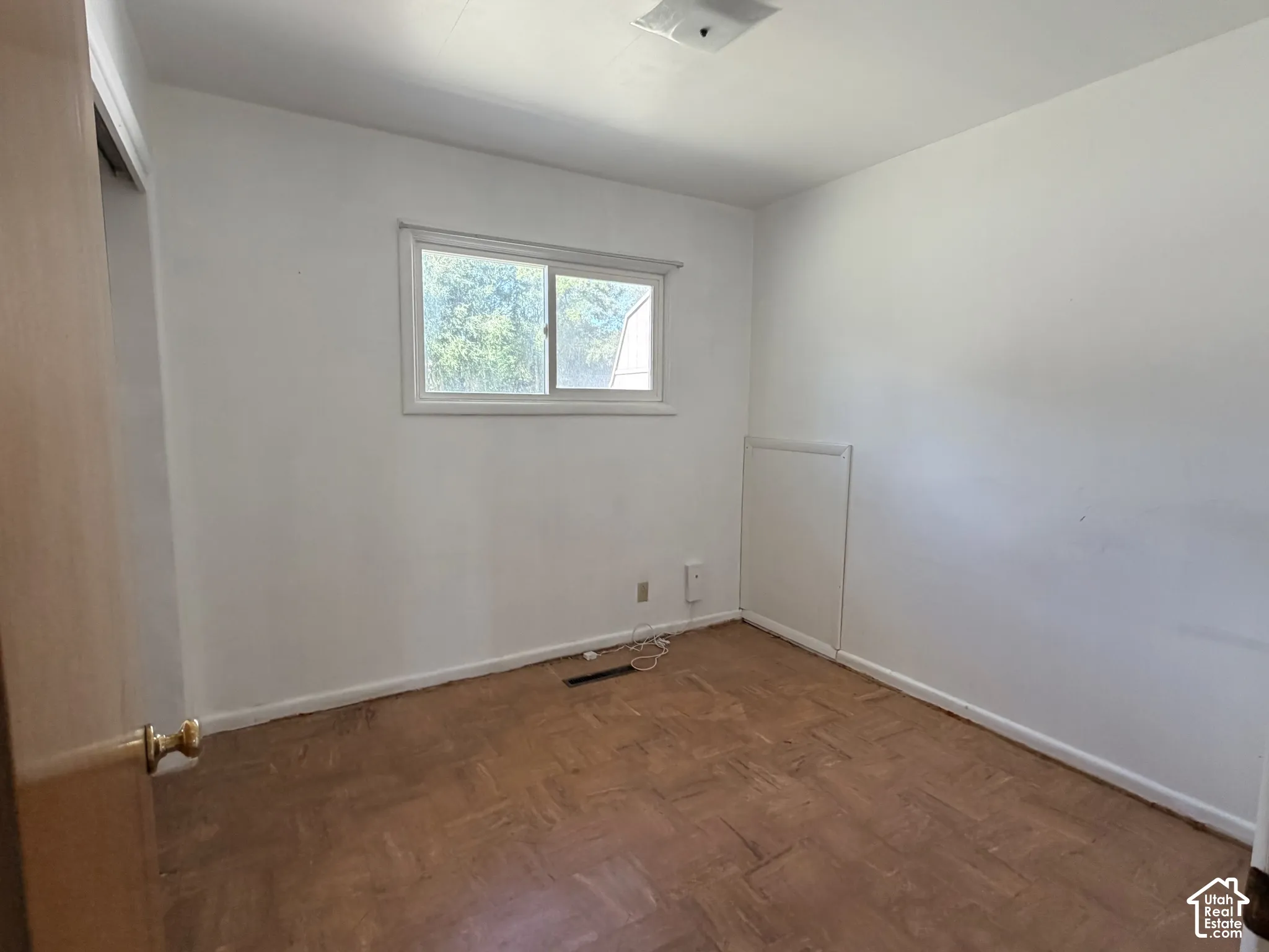 Interior space featuring wood-finish parquet flooring, white walls, a sliding window, and a built-in wall panel