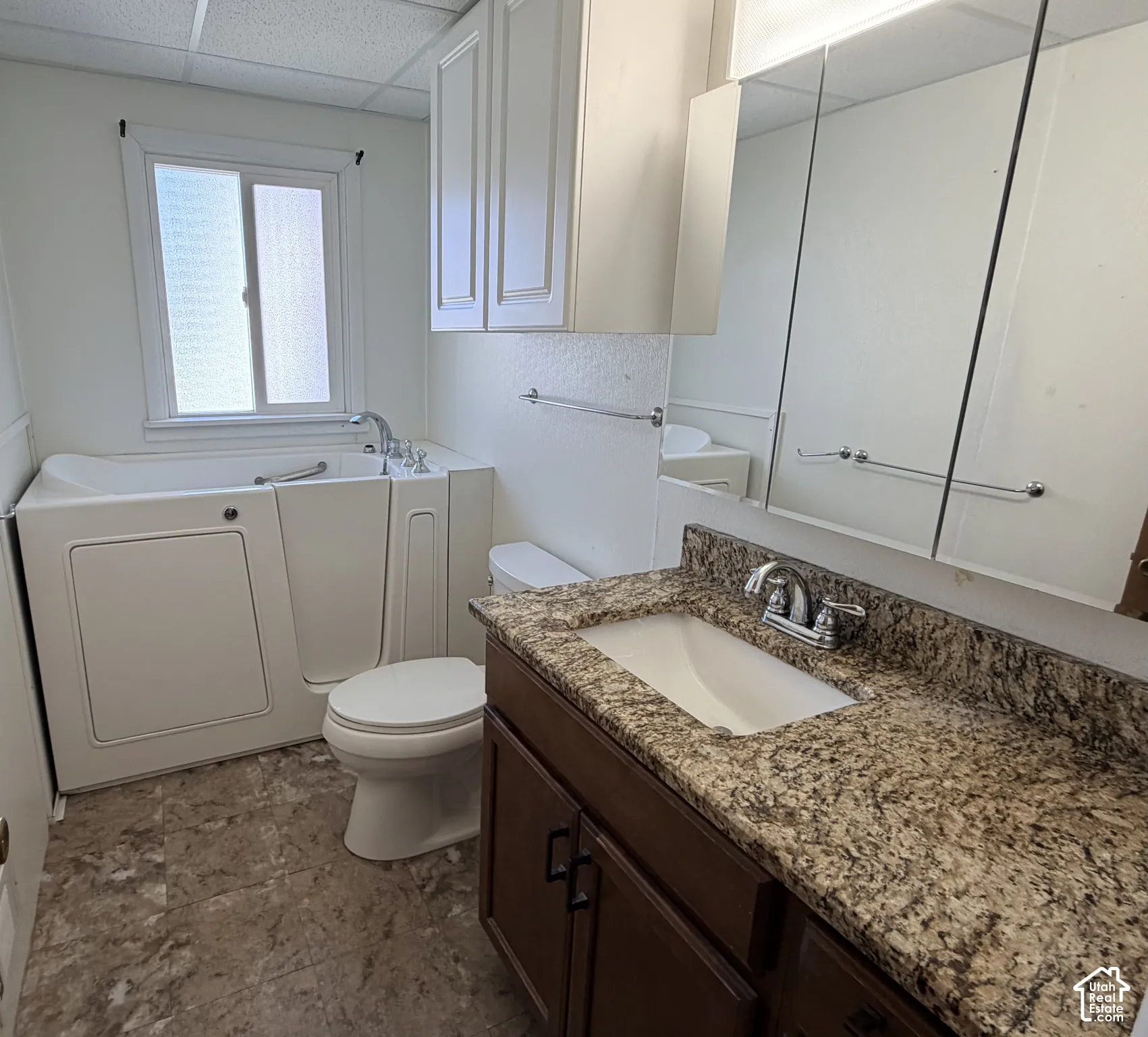 Bathroom featuring a walk-in tub, vanity with stone-finish countertop, under-mount sink, integrated wall-mounted mirrored cabinetry, and tile-finish flooring