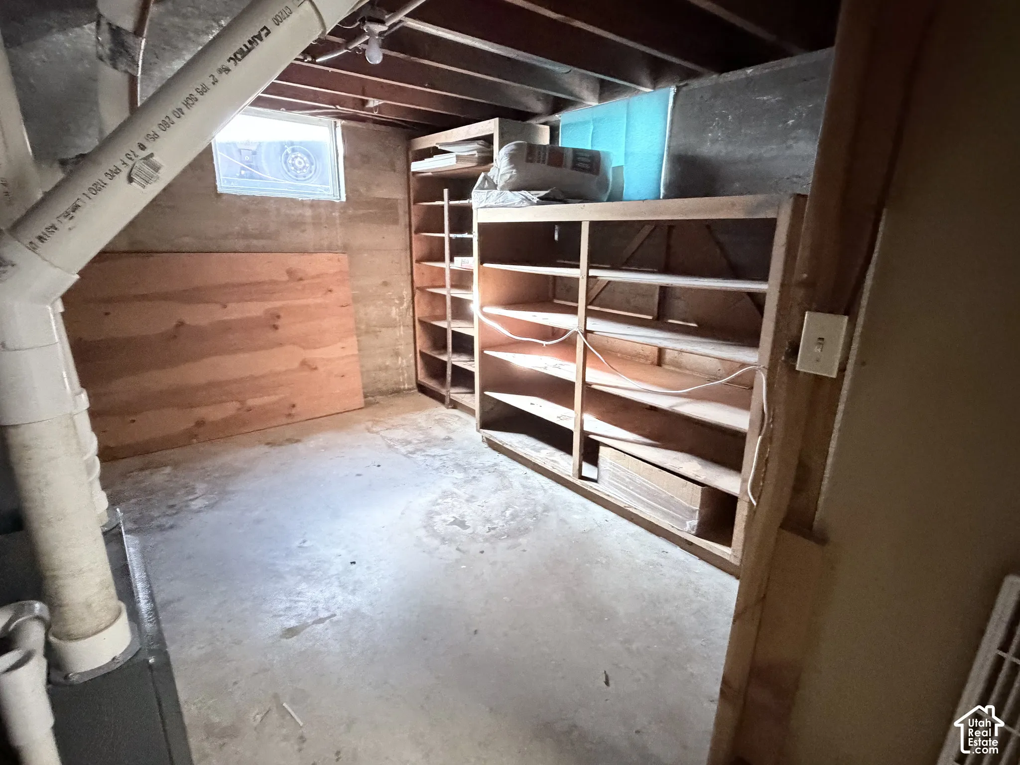 Unfinished storage space featuring concrete flooring, exposed wooden ceiling joists, concrete block walls, and built-in wooden shelving units