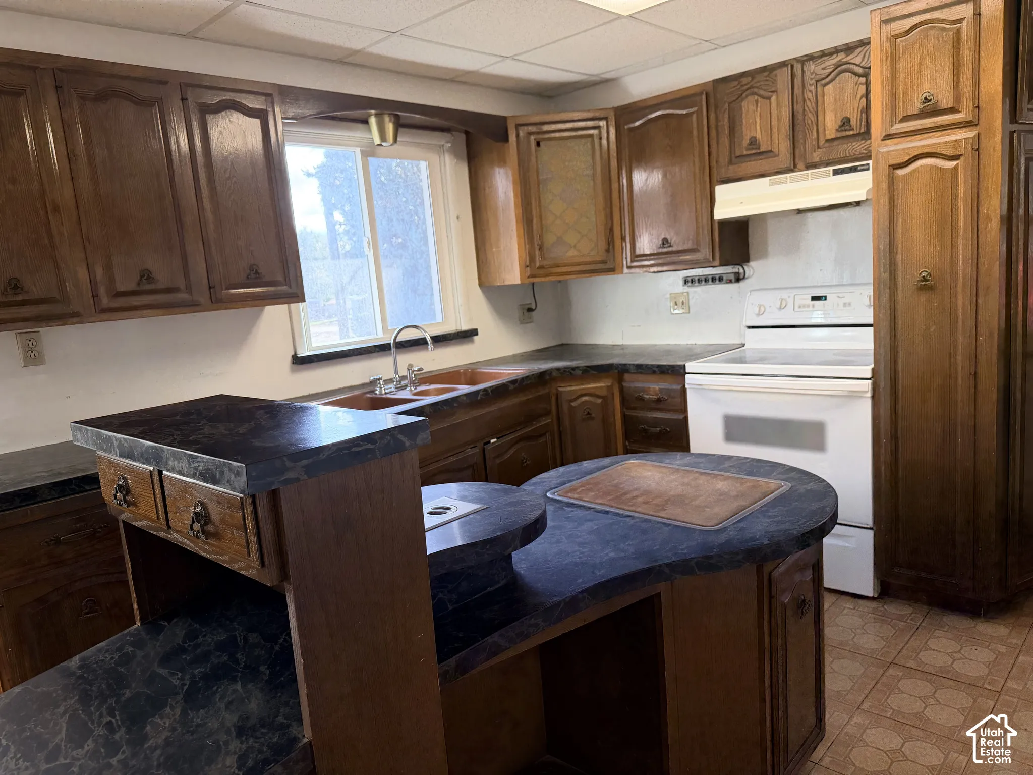 Kitchen featuring wood cabinetry, dark-finish laminate countertops, a dual-basin sink, an integrated island, and tile flooring