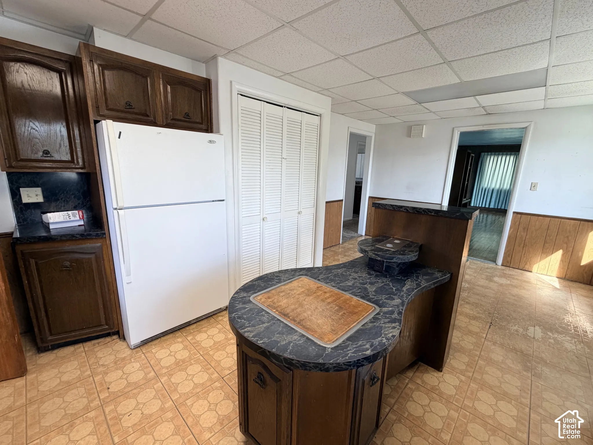 Kitchen featuring dark wood cabinetry, a tiered center island with dark patterned laminate countertops, ceramic tile flooring, and louvered double-door pantry closet