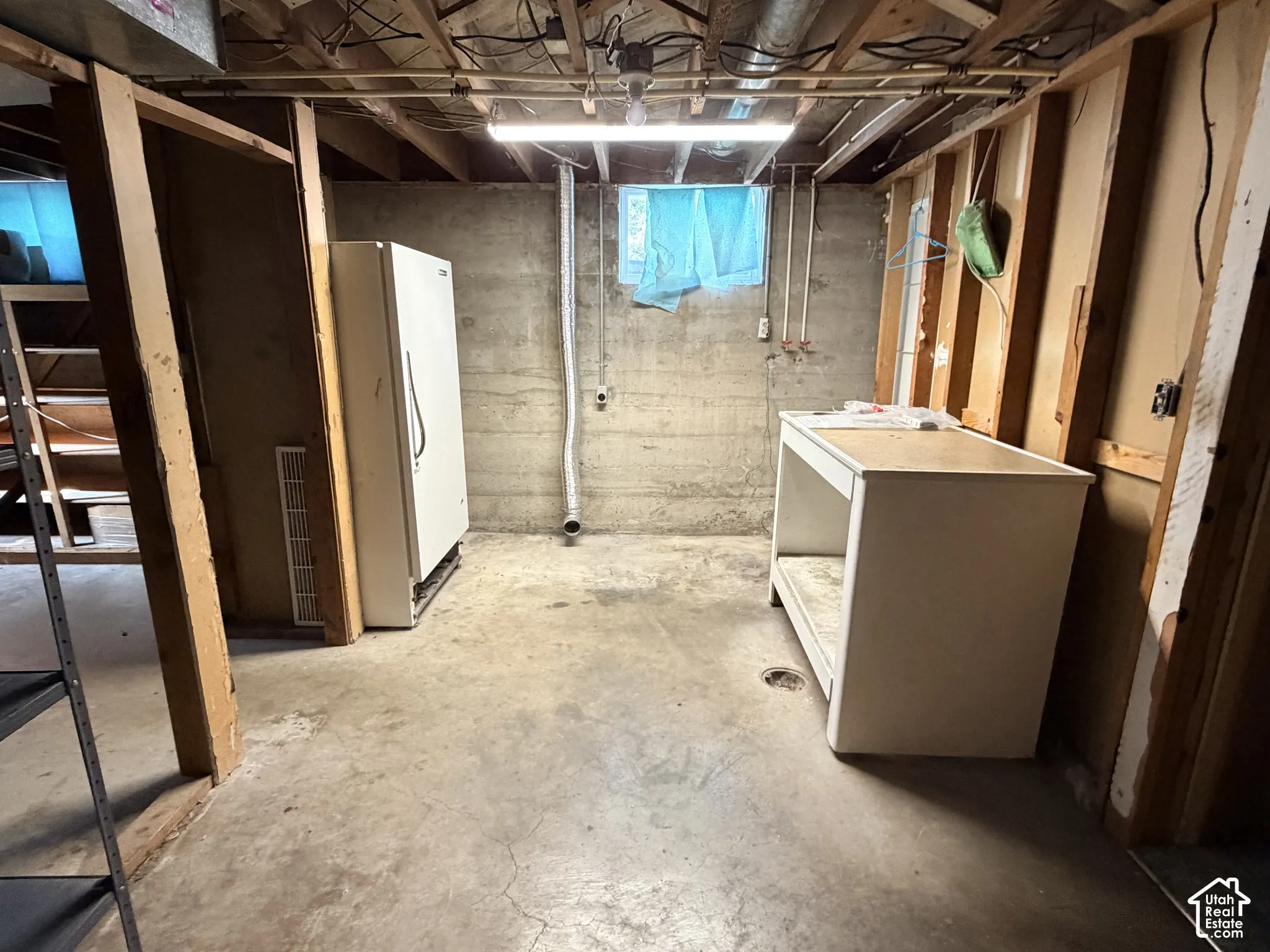 Unfinished lower level utility space featuring exposed wood framing, concrete foundation walls, concrete floor, built-in counter, and fluorescent lighting