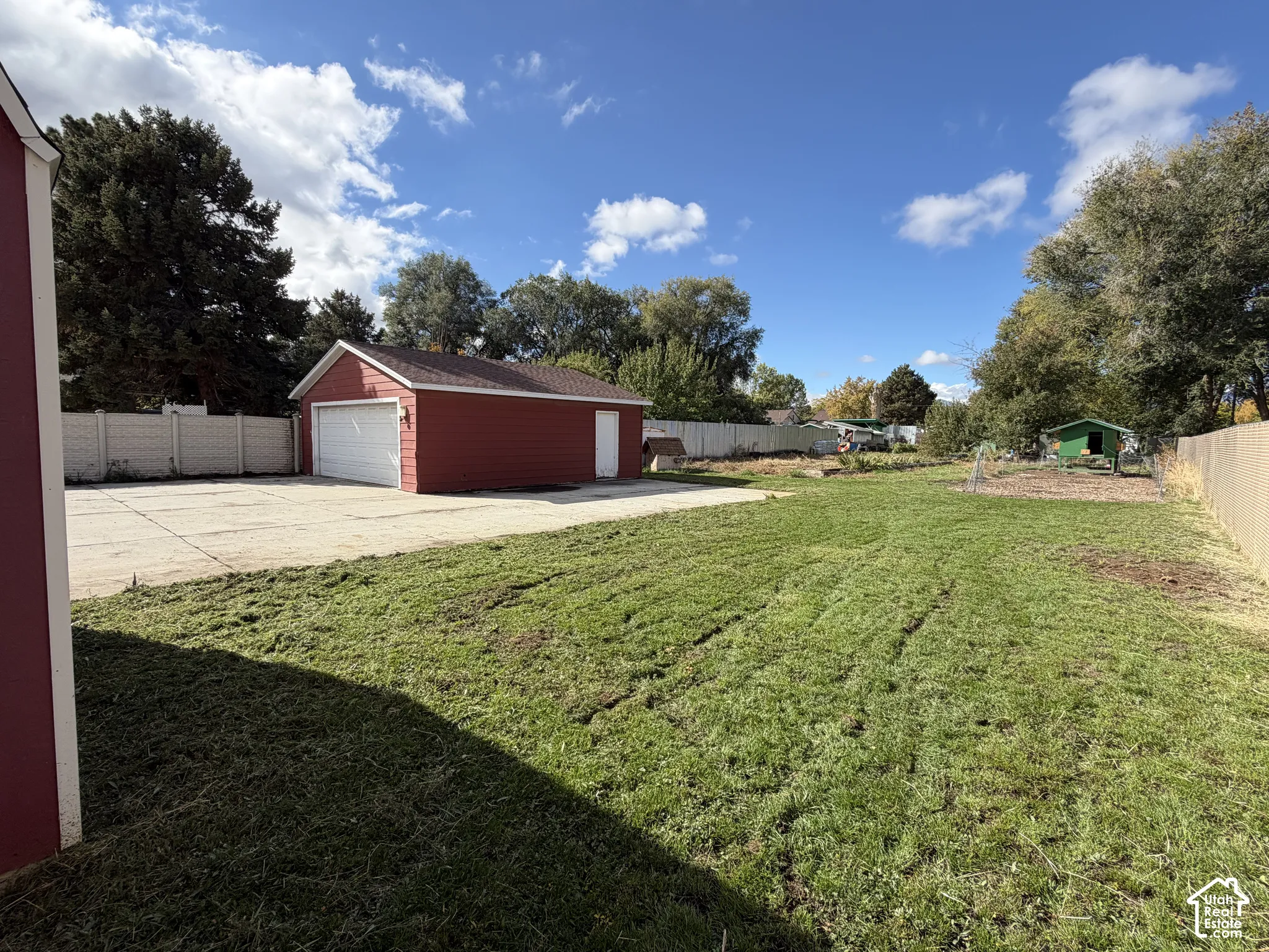 Expansive backyard featuring a detached garage, concrete parking pad, perimeter fencing, and mature trees