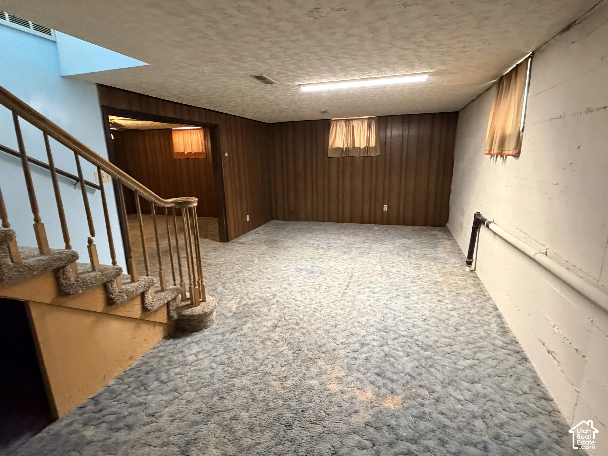 Open-plan interior featuring wood-paneled walls, carpeted flooring, a staircase with a wooden railing, and recessed ceiling lighting
