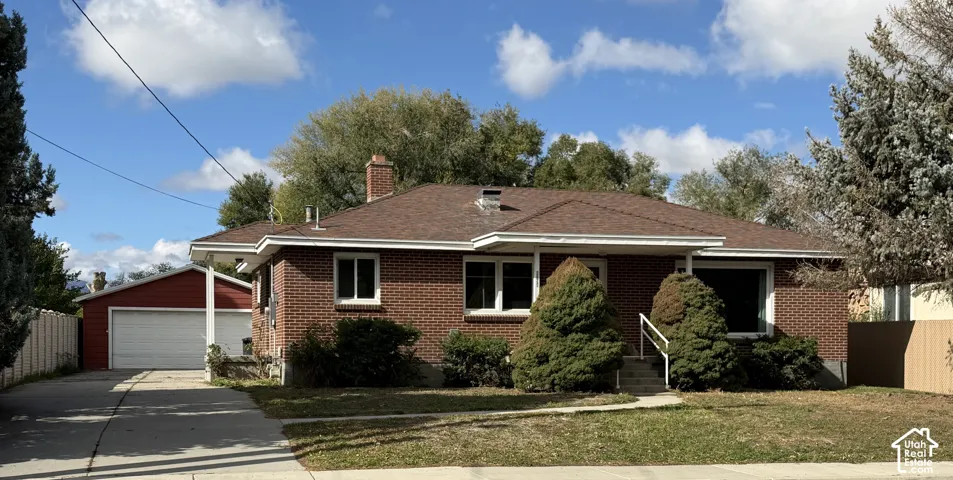 Brick exterior featuring a hip roof, chimney, detached garage, and concrete driveway