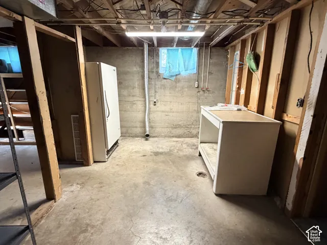 Unfinished lower level utility space featuring exposed wood framing, concrete foundation walls, concrete floor, built-in counter, and fluorescent lighting