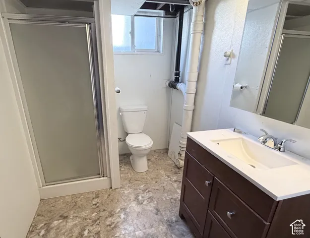Bathroom featuring a glass-enclosed shower, white porcelain toilet, vanity with a white countertop and integrated sink, and patterned resilient flooring