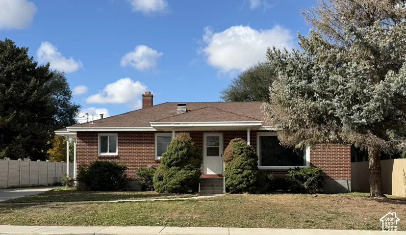 Brick exterior facade featuring a covered entryway, chimney, asphalt shingle roof, and large front-facing windows