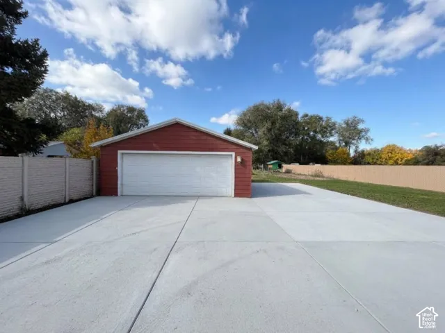 Detached garage with horizontal siding, expansive concrete apron, and surrounding masonry and solid-panel fencing