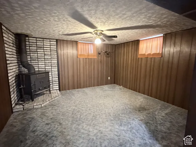 Wood-paneled walls, floor-to-ceiling painted brick accent wall, freestanding iron stove, textured ceiling, and central ceiling fan