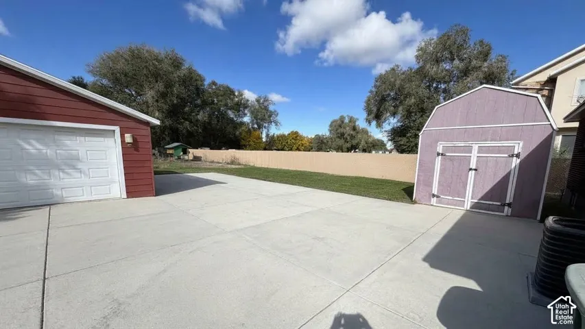 Concrete driveway, detached storage shed, exterior wall fencing, and multi-car garage