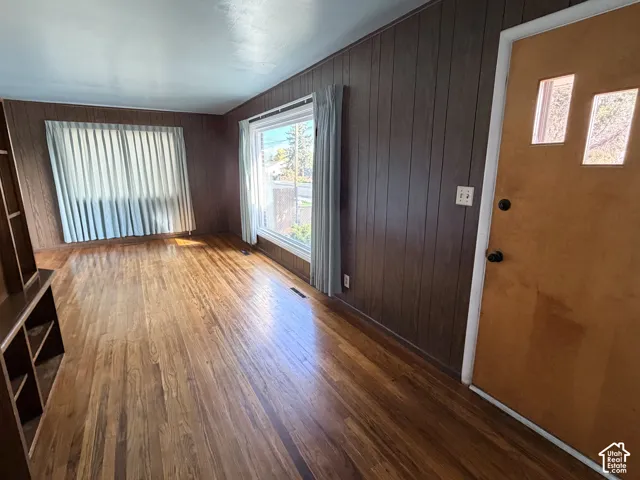 Interior space featuring wood-finish flooring, dark wood-paneled walls, large windows, and a natural-finish wood door with dual rectangular glass inserts