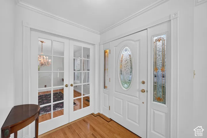 Entryway featuring wood-finish flooring, white paneled double doors with glass lites, and an exterior door with decorative leaded glass inserts and sidelights