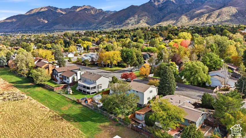 Aerial perspective featuring a prominent mountain backdrop, mature trees, established neighborhood streets, and expansive open space