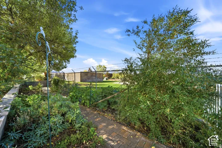 Landscaped garden featuring brick paver walkways, mature plantings, and perimeter chain-link fencing