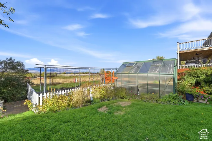 Backyard featuring a greenhouse, a fenced garden area with metal trellising, a manicured lawn, and an elevated deck with a wooden railing