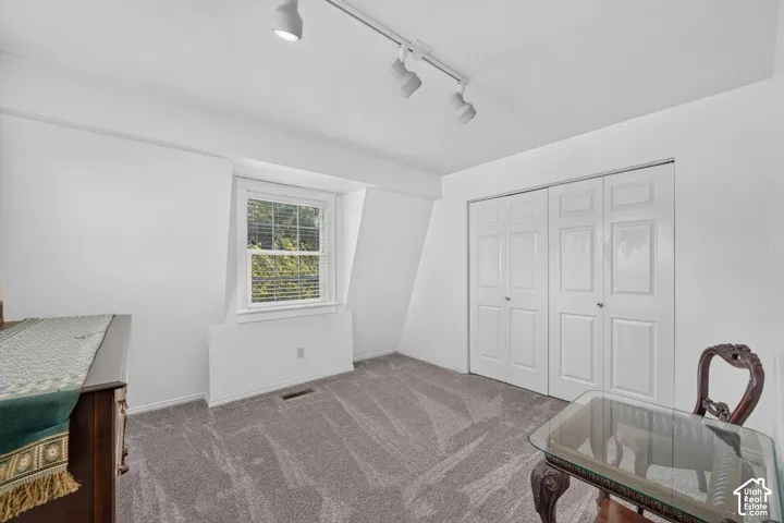 Neutral-toned carpeting, dual-pane recessed window, multi-panel closet doors, and adjustable overhead track lighting