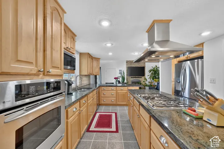 Kitchen featuring natural wood cabinetry, stone-surface countertops, built-in stainless steel wall oven, gas cooktop with stainless steel range hood, and tile flooring