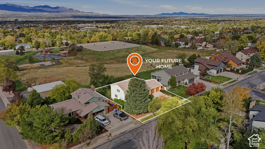 Aerial perspective of a detached residential property featuring a shingle roof, multi-car garage, established mature trees, and a mountain backdrop