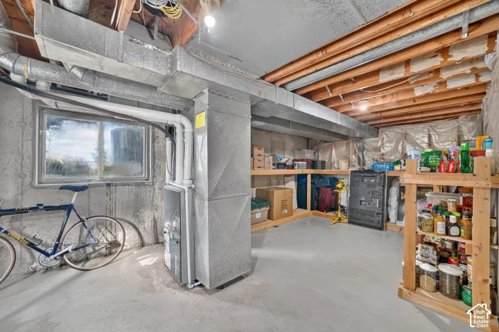 Lower level utility space featuring exposed wooden joists, poured concrete walls, a sliding glass window, and built-in wood shelving units