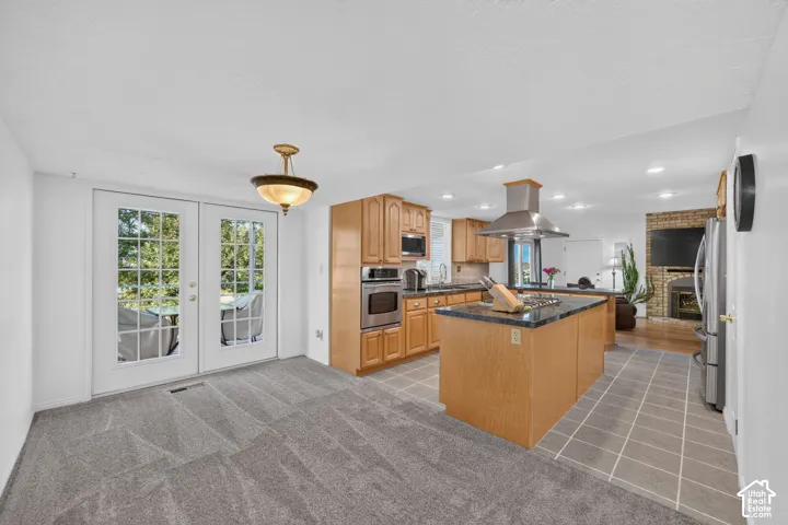 Kitchen featuring wood cabinetry, stainless steel wall-mounted oven, central island with stone-finish countertop, stainless steel range hood, and tile flooring