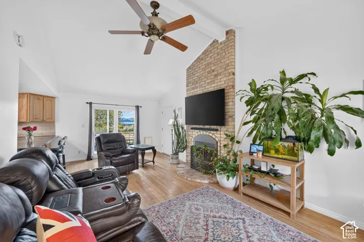 Vaulted ceiling featuring a central wood-blade ceiling fan, floor-to-ceiling brick fireplace with a curved hearth, and light-toned wood-finish flooring