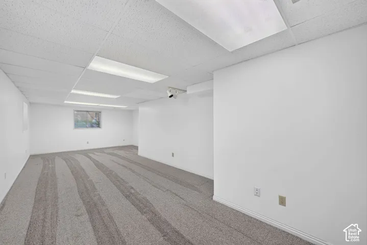 Expansive interior space featuring neutral wall-to-wall carpeting, recessed ceiling panels, integrated overhead lighting, and a window