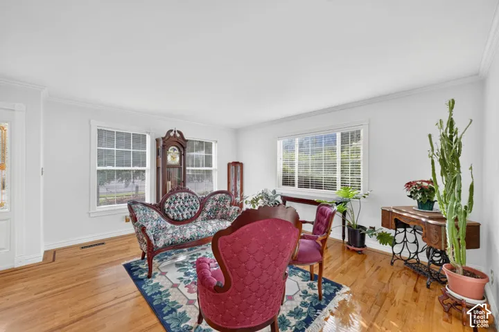 Living area featuring hardwood flooring, crown molding, and large windows with horizontal blinds